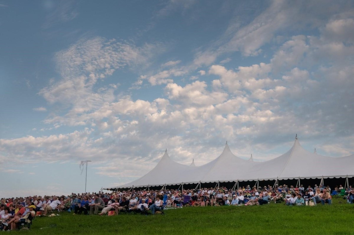 People in a grassy field and a white tent