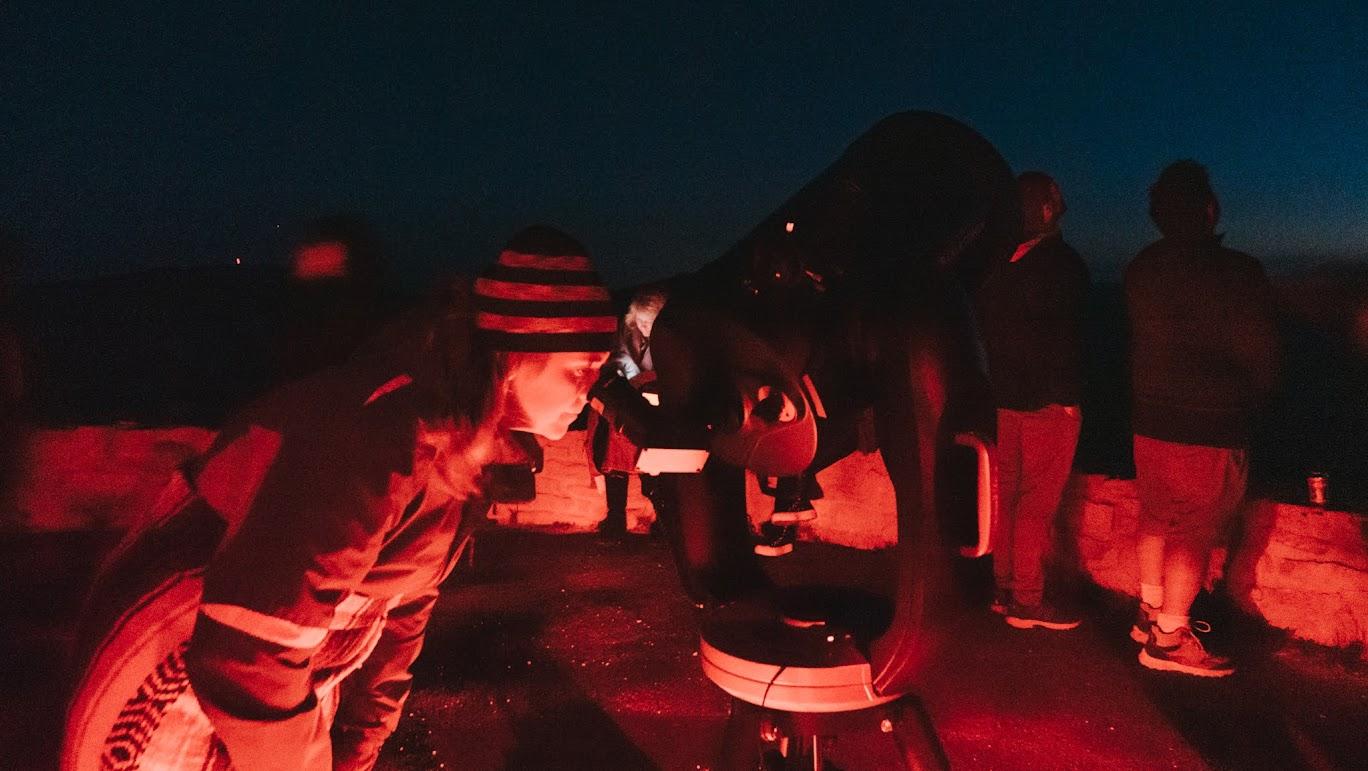 A visitor peers through a telescope under red light during a Night Sky Tour at Cedar Breaks.