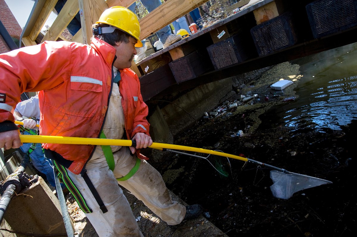 A man with a long net gets trash out of a canal