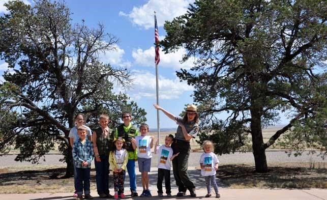 A female park ranger standing in front of a flagpole wth seven children standing around her