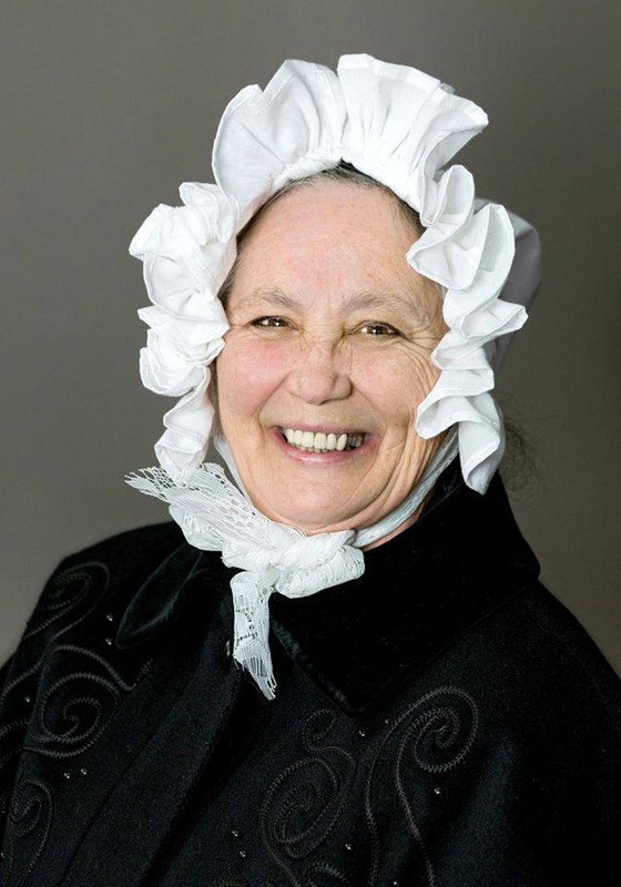 Image of a white women wearing colonial dress and a bonnet smiling at the camera