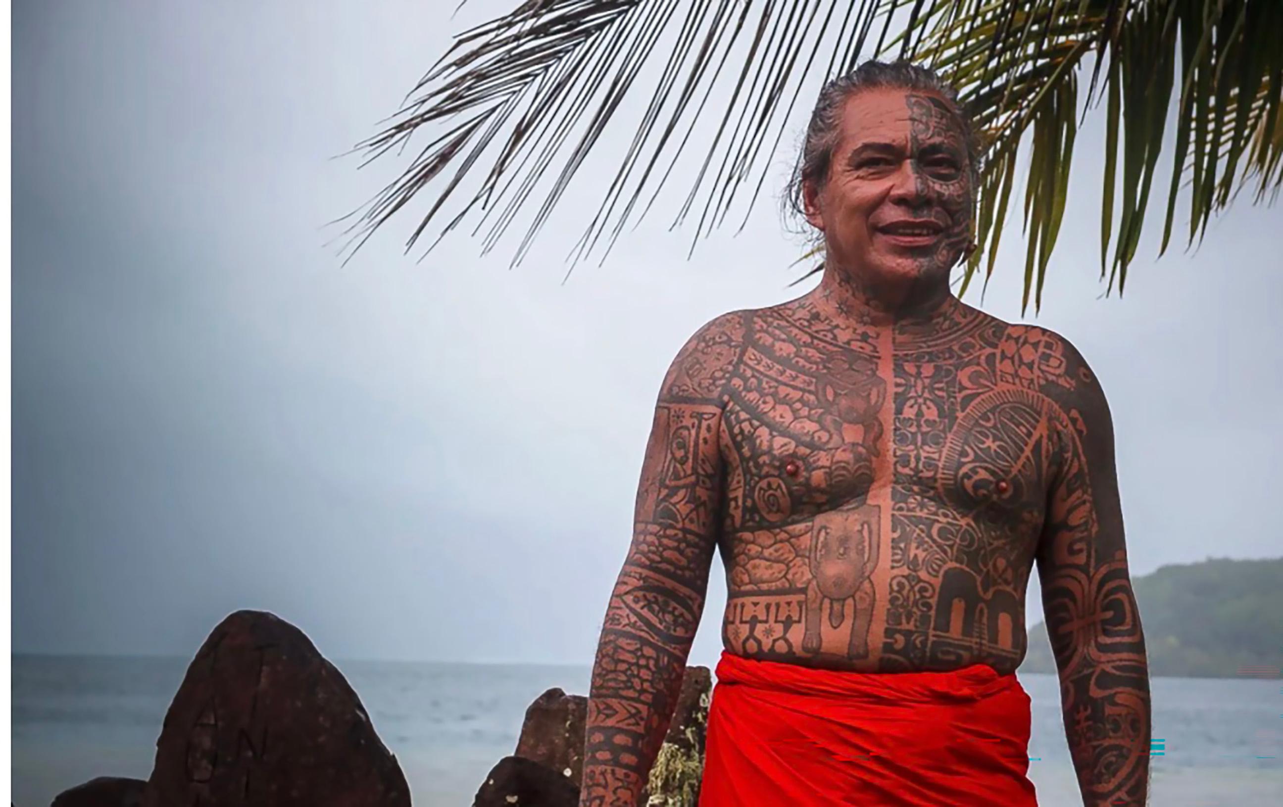 Man with tattoos, with ocean and coconut fronds in the background