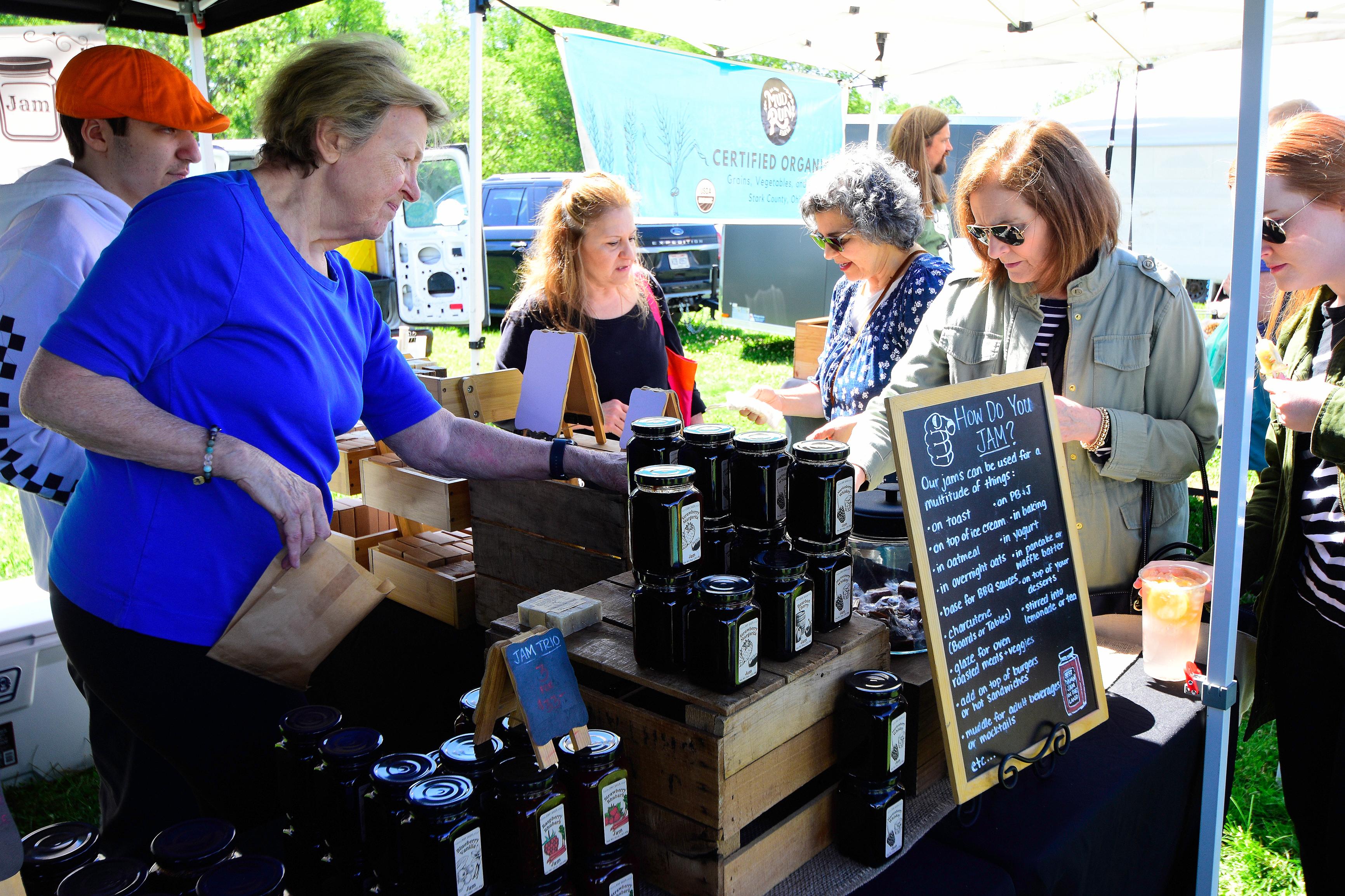 Shoppers look over different options of jam jars at a Farmers Market booth.