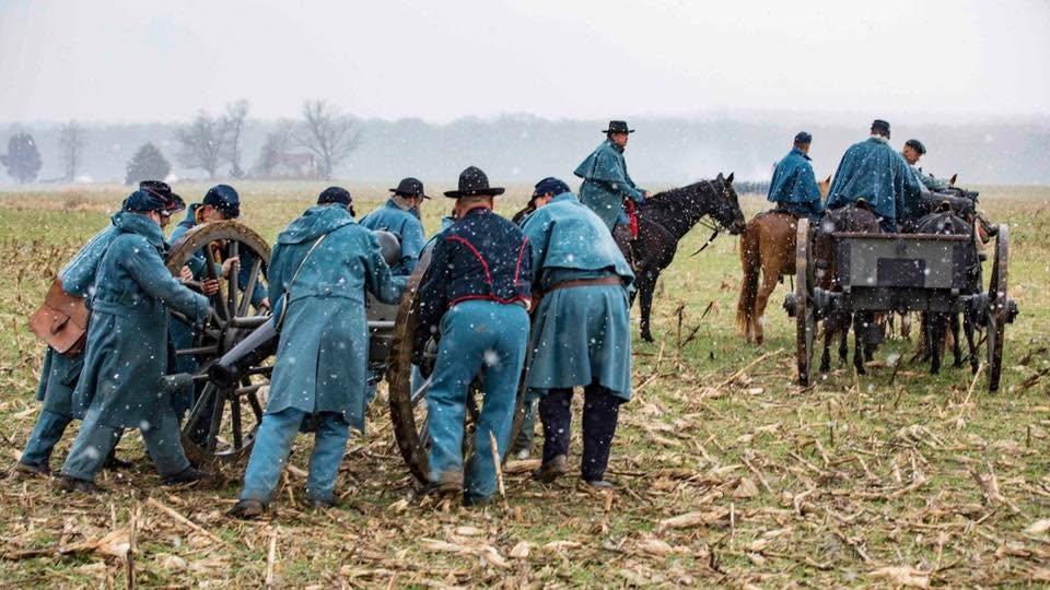 Civil War living historians gather around a cannon and horses on a snowy winter day.
