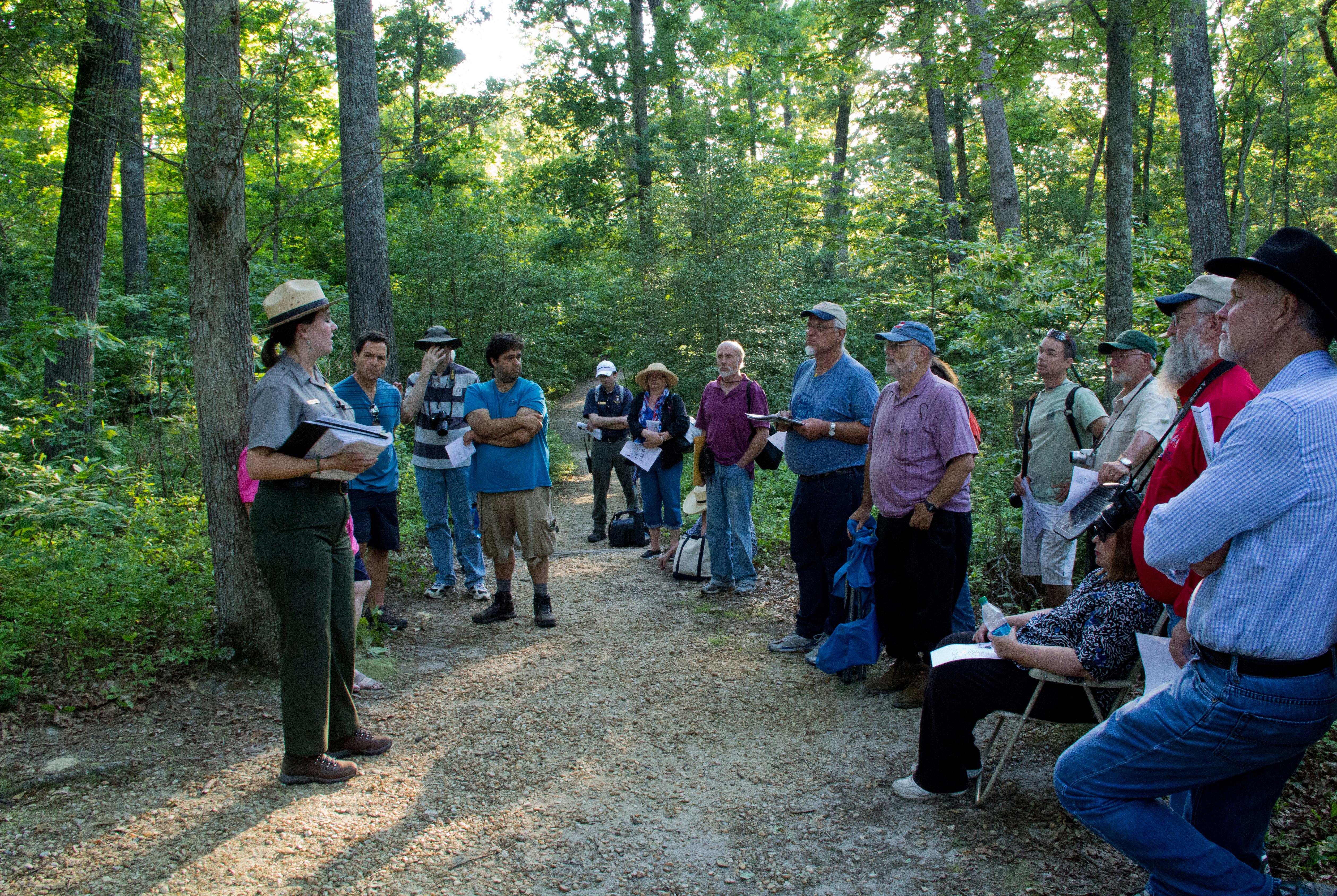 A park ranger addressing a group of visitors in a shady, wooded area.