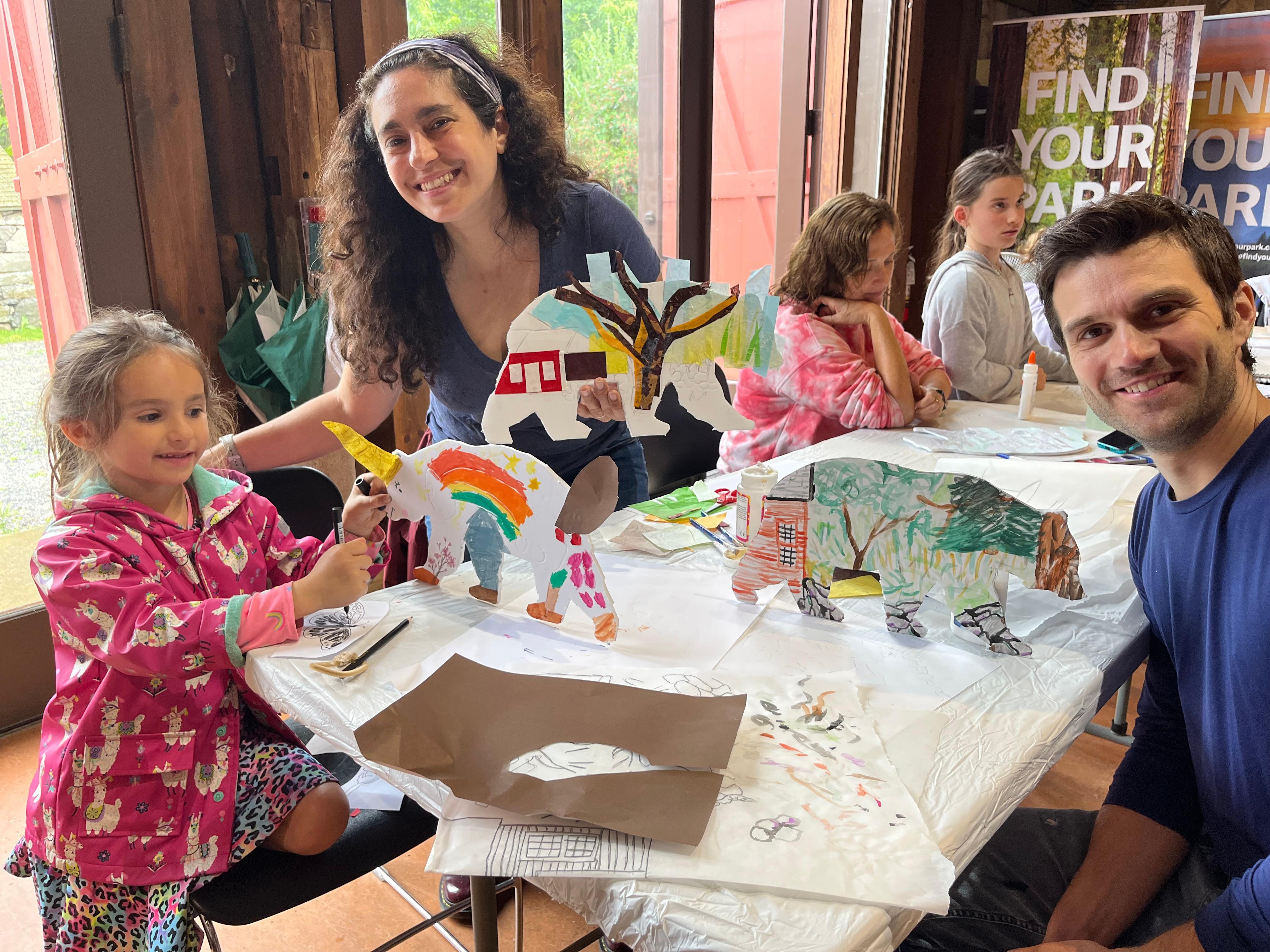 A group of people (a woman, a man, and a child) sitting at a table with three colorful art bears.