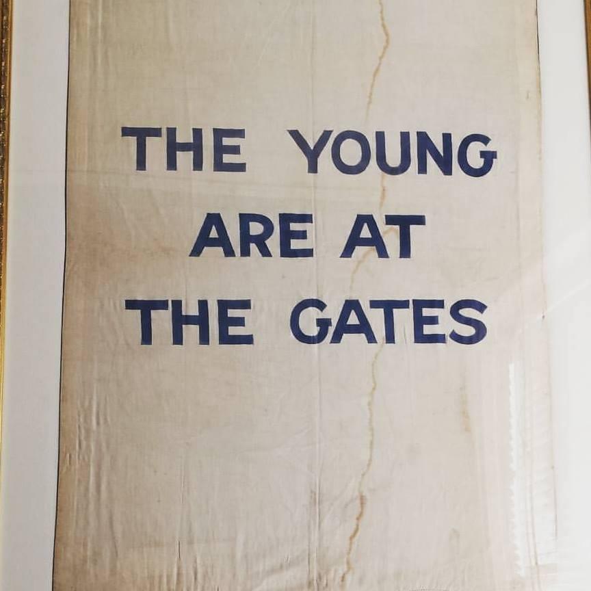 Framed suffrage banner in museum exhibit with block letters: The Young Are At The Gates