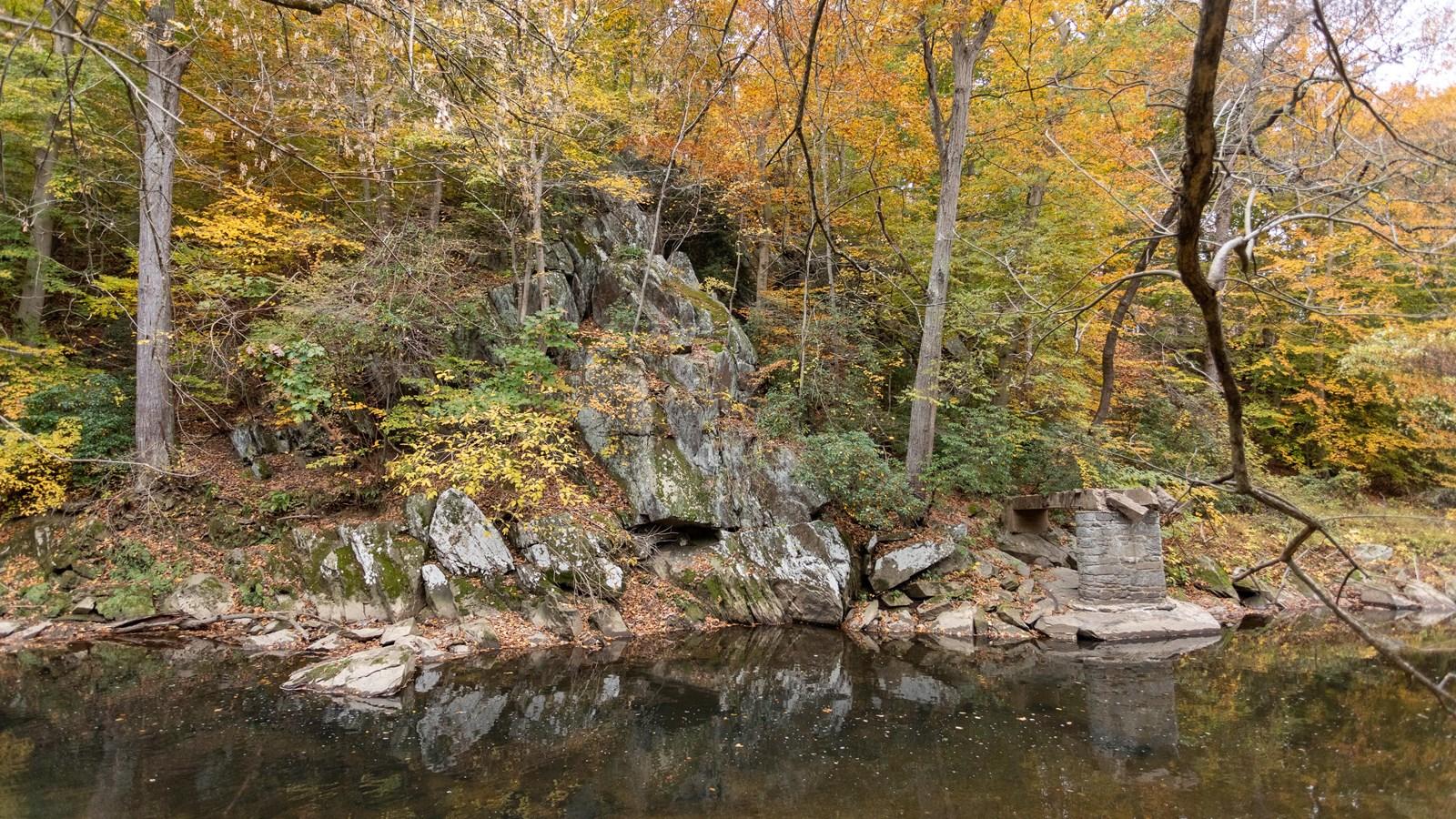 A large rockface sits above a creek, surrounded by trees and fall foliage