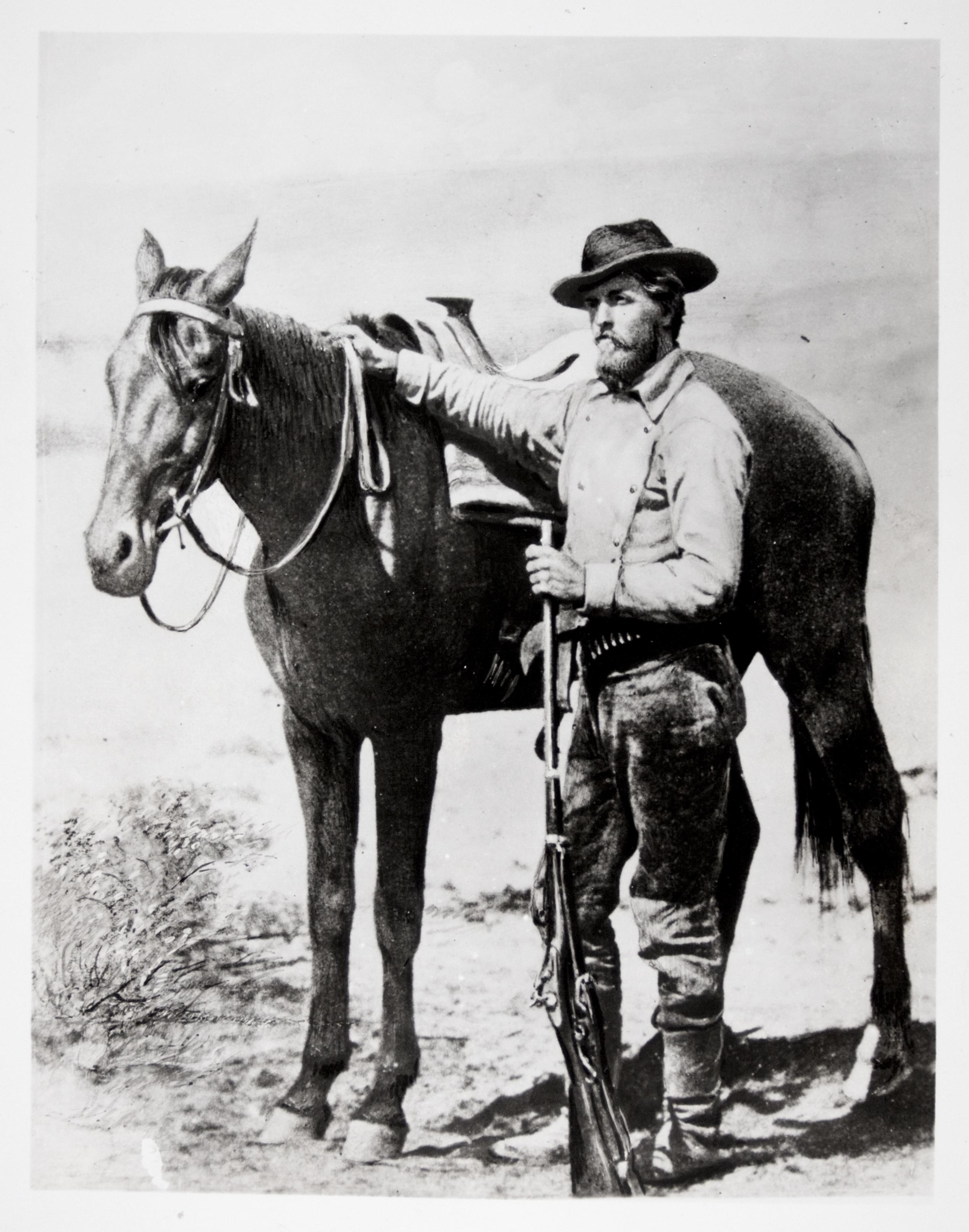 A black and white photograph of a young man holding standing next to a horse.