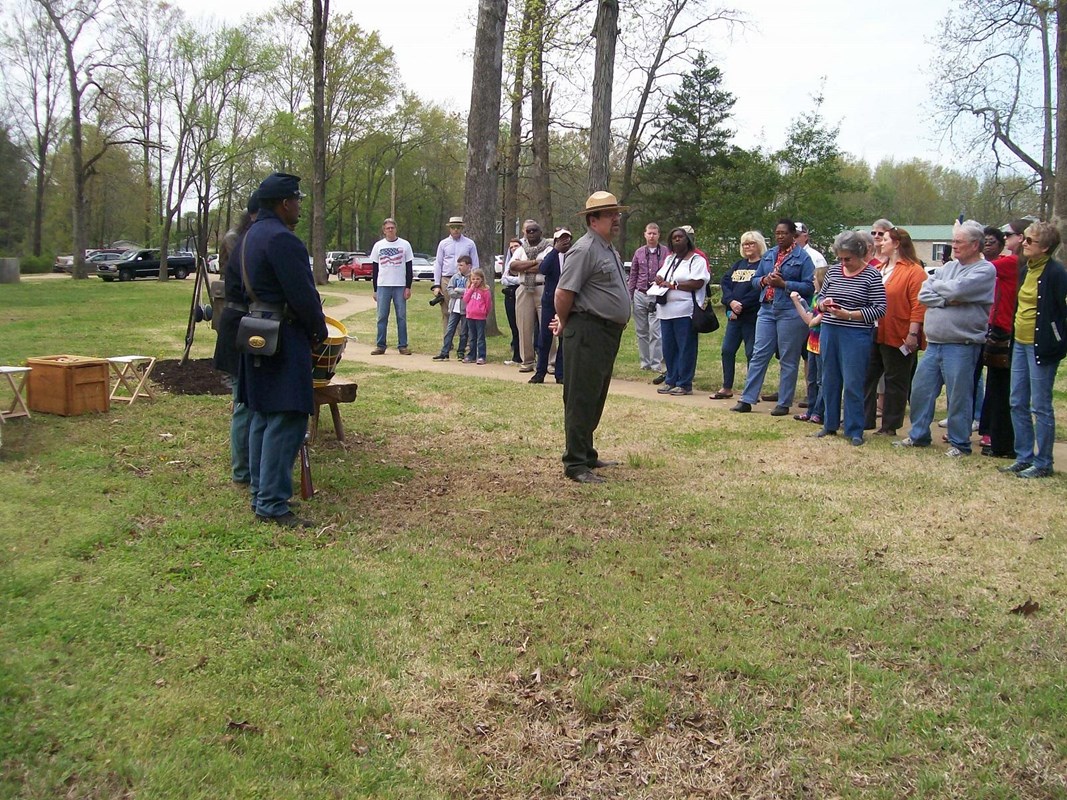 A park ranger in green and gray talks to a crowd.
