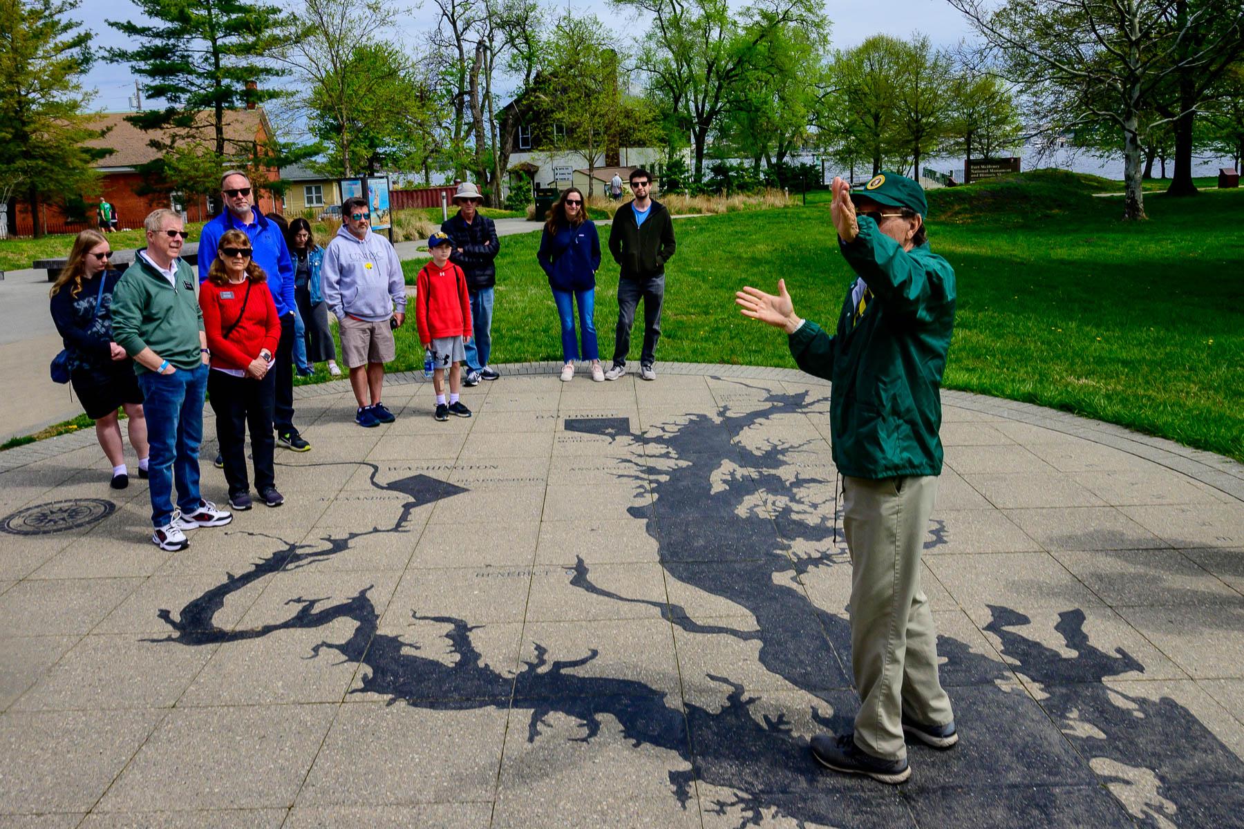 Volunteer talking to a group of visitors on a stone map of the chesapeake.