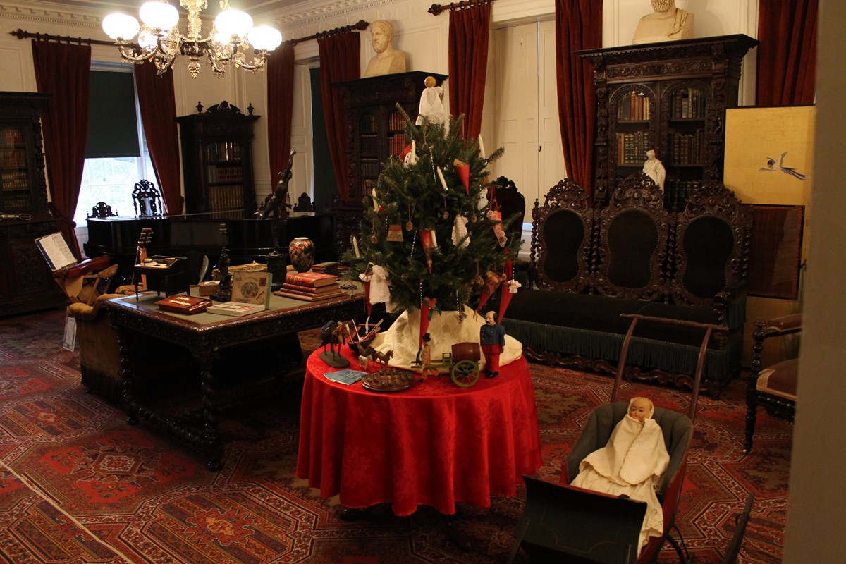 large room with Victorian decor, decorated for Christmas with a tabletop tree and presents below