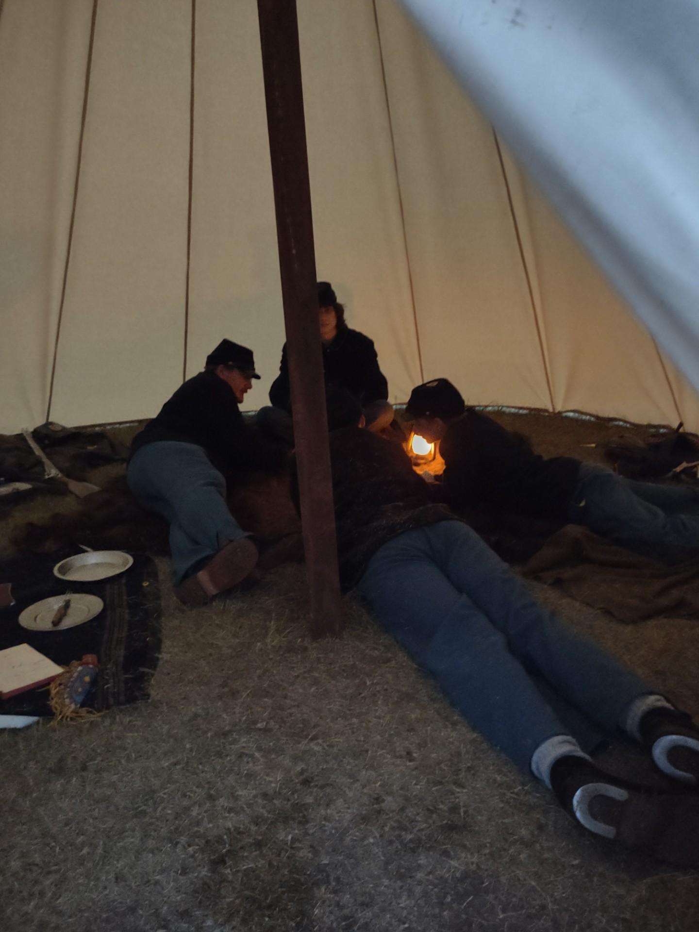 Image of three soldiers inside a tent huddled around a candle