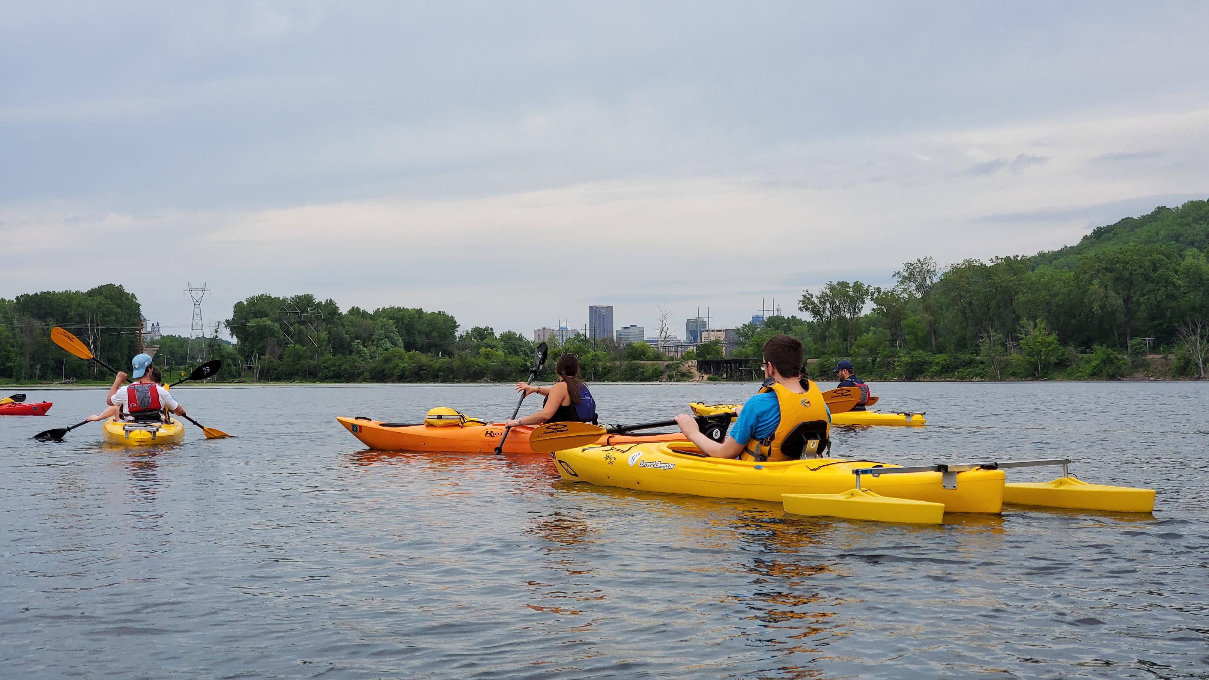 Kayakers sit in a lake with a downtown skyline in the background