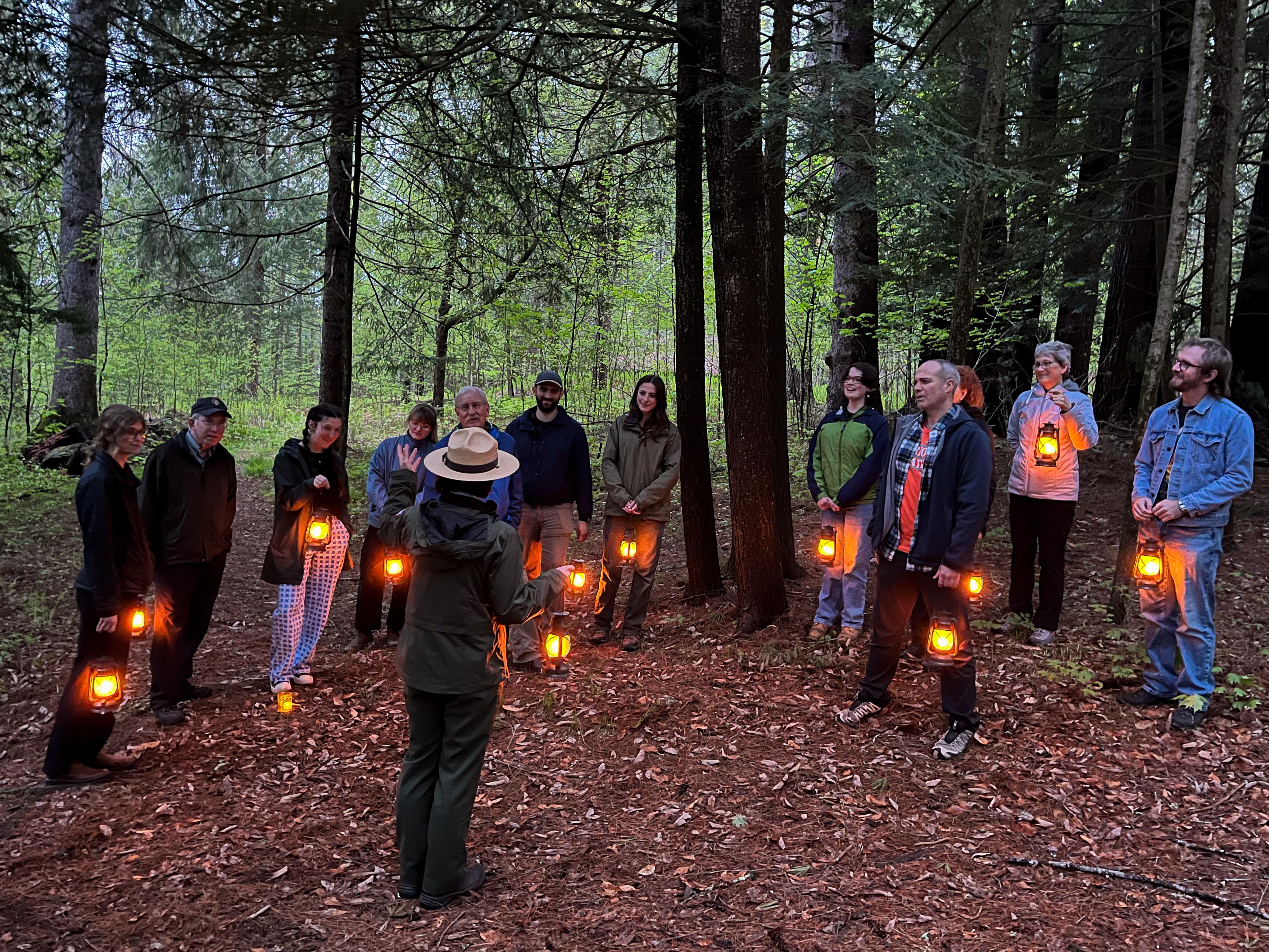 Park Ranger talks to group at dusk in the forest, all parties are holding laterns