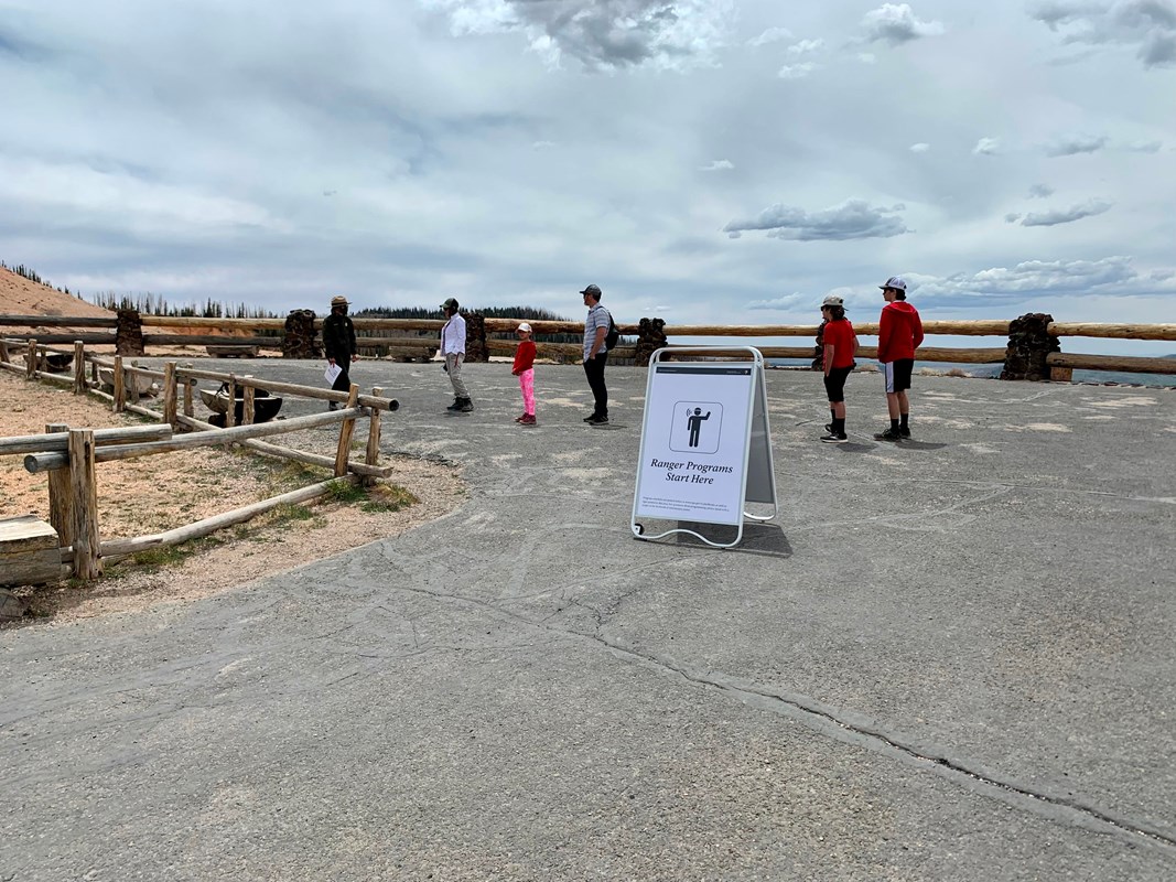 A ranger speaks to several people at an overlook surrounded by wooden fencing.