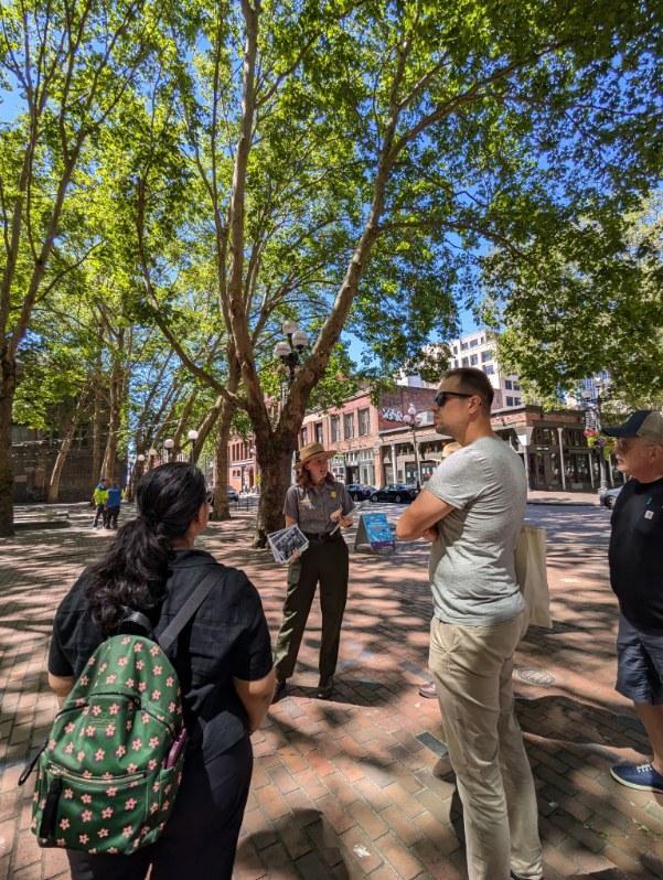 Ranger talking with visitors outside in a city neighborhood with trees behind and holding a historic