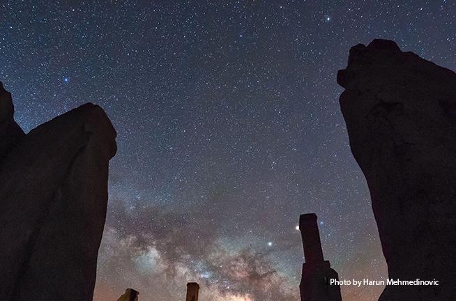 Towering adobe walls with a star-filled sky in backgound and white haze of Milky Way.