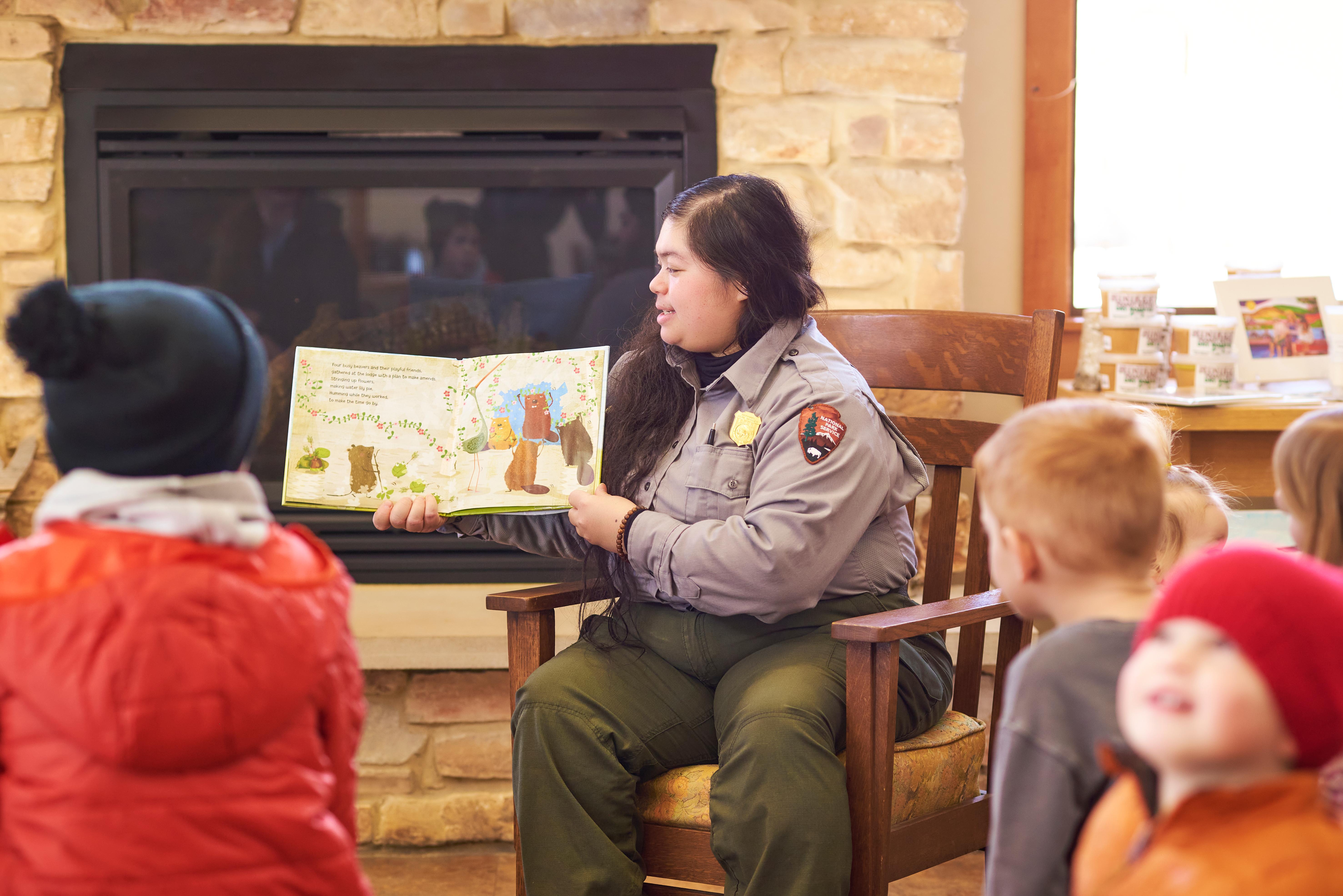 A park ranger holds a children's book while reading to a youth audience