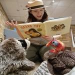 a uniformed ranger with a hat reads a book to puppets.