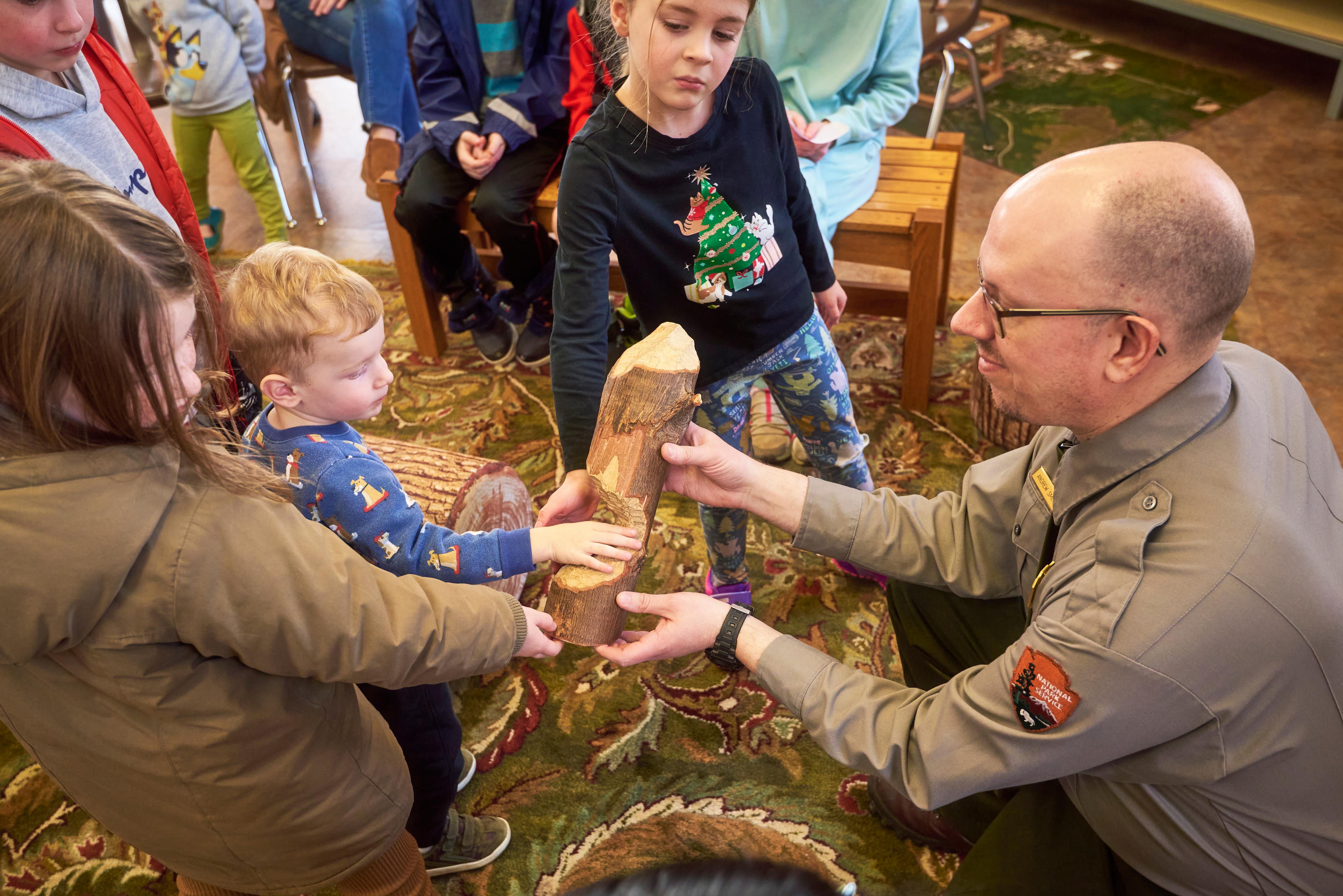 A park ranger holds a log chewed by a beaver for young visitors to touch