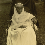 An aged Harriet Tubman wearing a white shawl and seated in a high back chair.