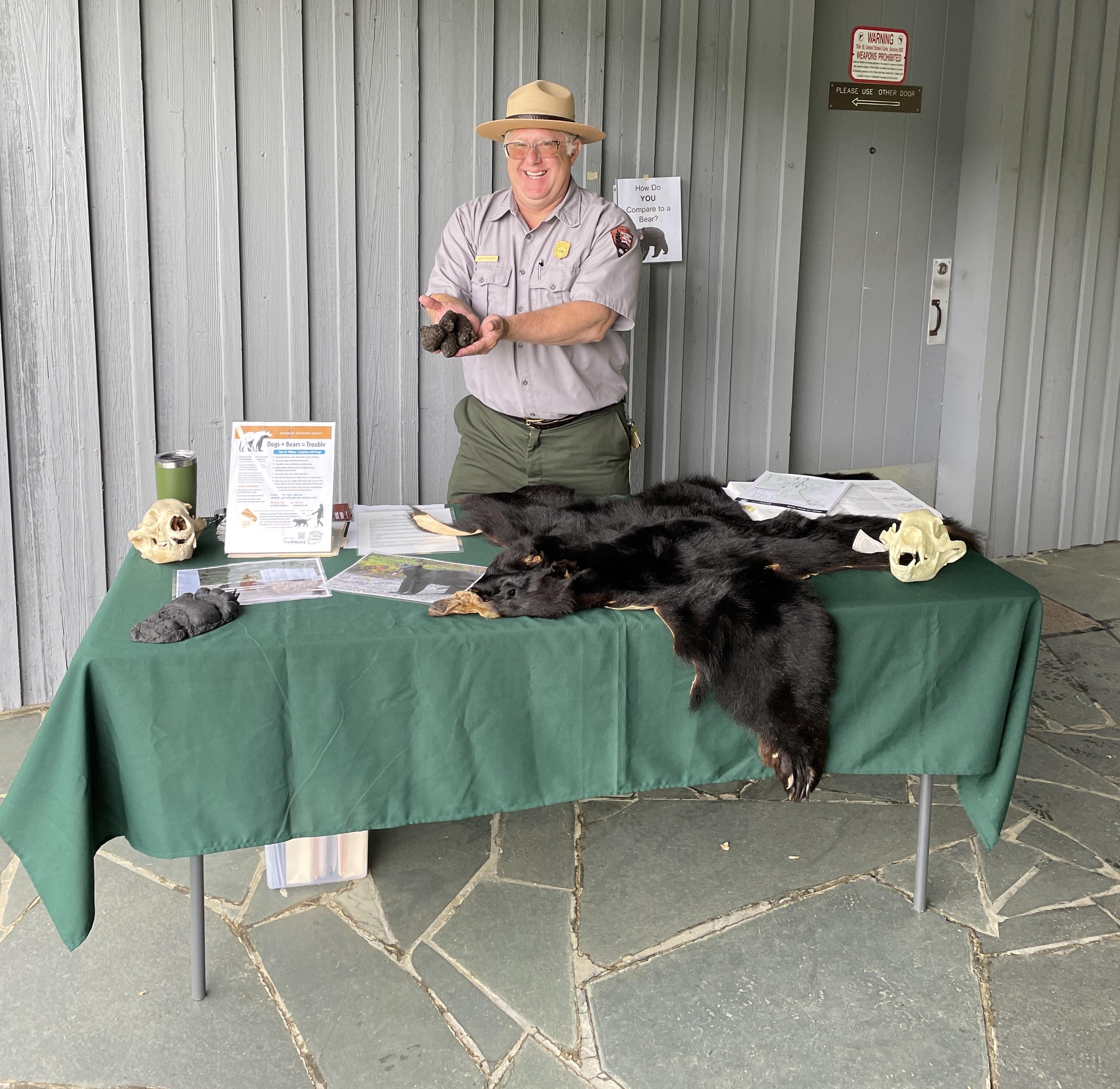 Man behind a table with a bear fur and skulls holds out a mold of bear poop.