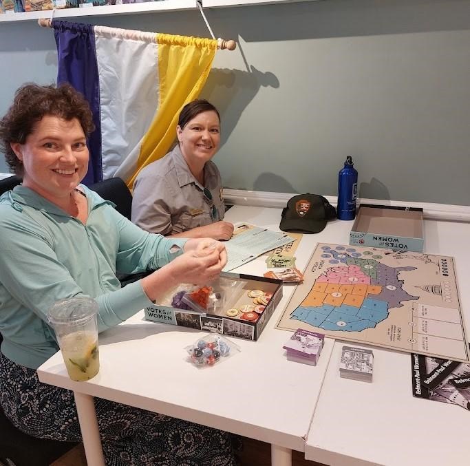 Two people playing the Votes for Women Game with a suffrage banner hung behind them