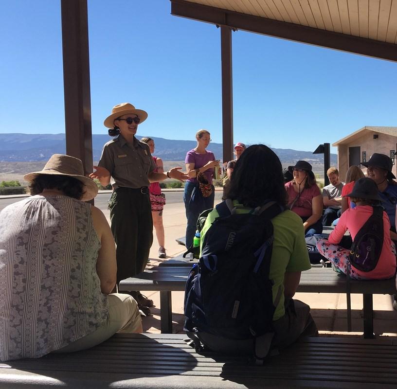 A ranger in a flat hat gestures at the hills and mountains of Dinosaur. A small crowd watches