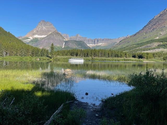 view overlooking lake surrounded by forest and mountain with blue sky and a distant white tour boat