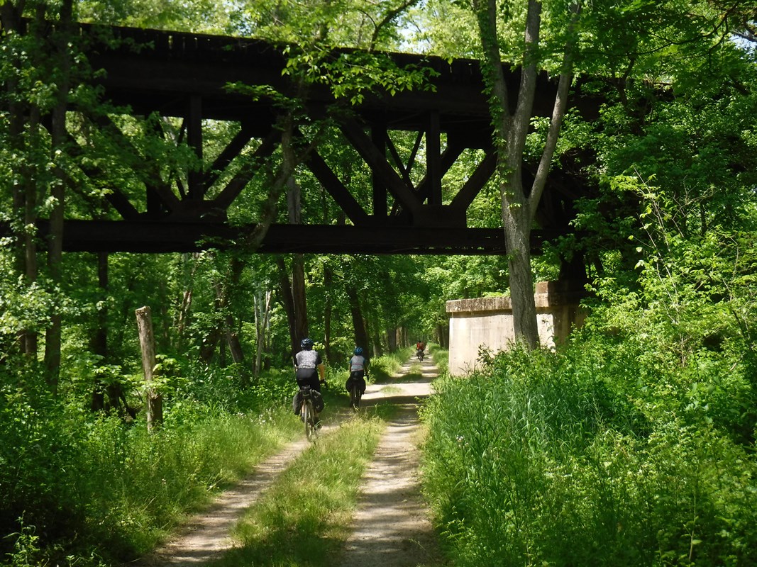 Bicyclist riding on towpath passing a railroad bridge above them