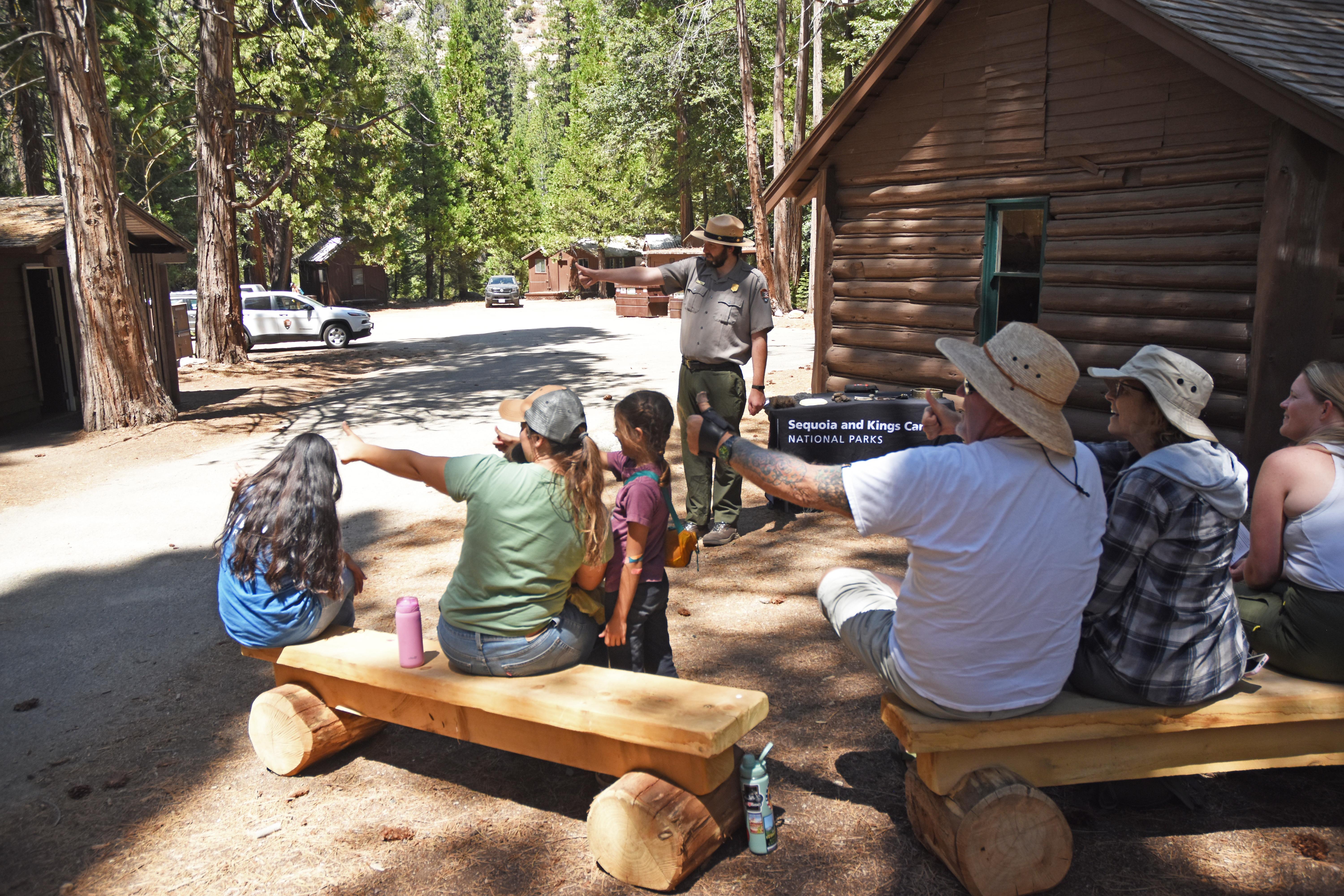 A park ranger talks to a group of visitors in front of a rustic cabin.
