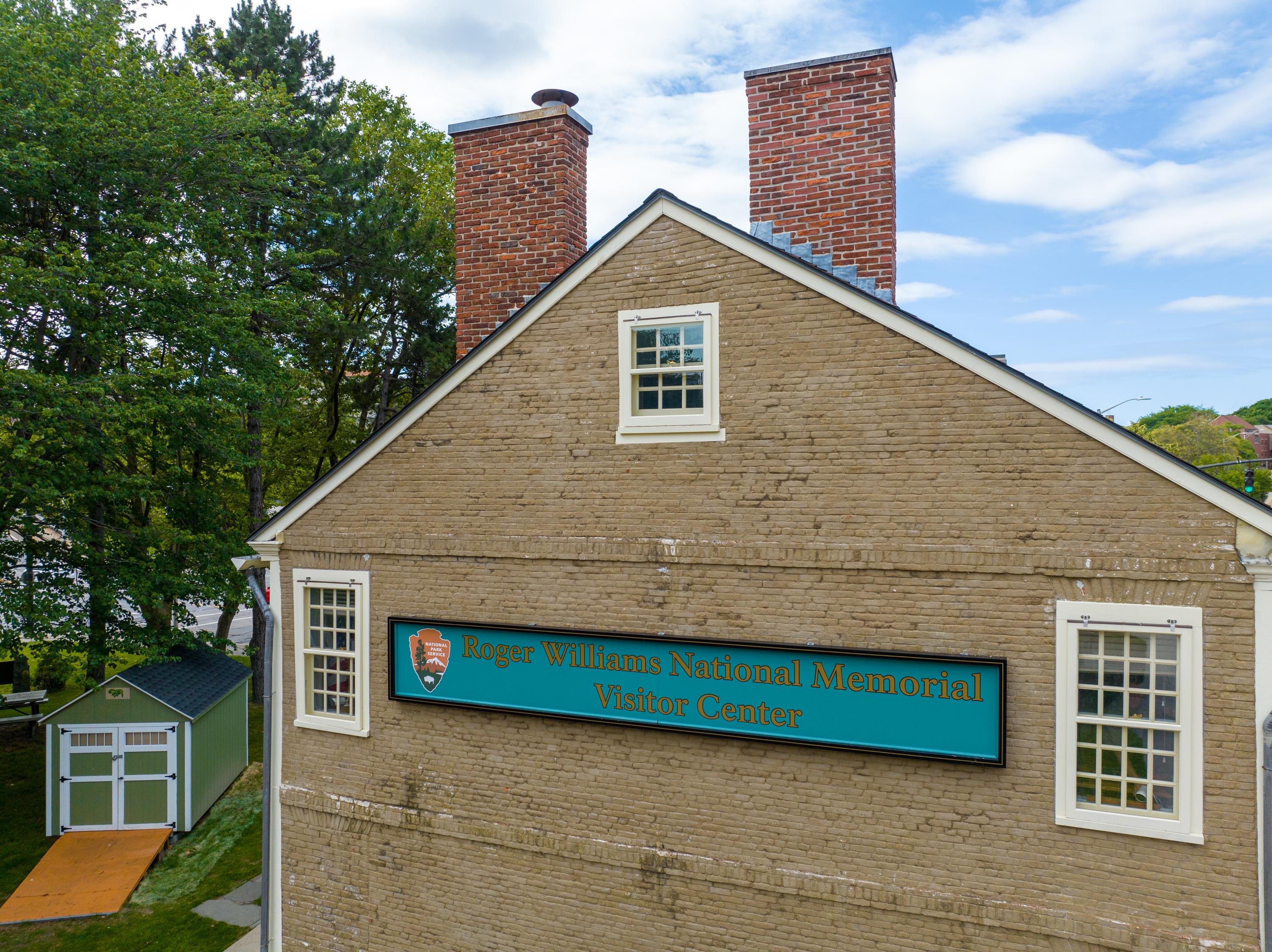 The side of a stone building with two chimneys and trees in the background