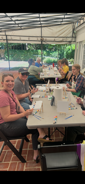Group of people seated at a table on an outside terrace with painting supplies