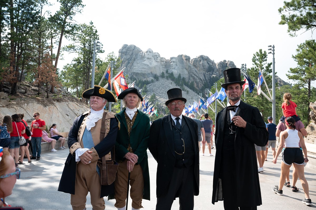 Presidential re-enactors pose for a photo with Mount Rushmore in the background.