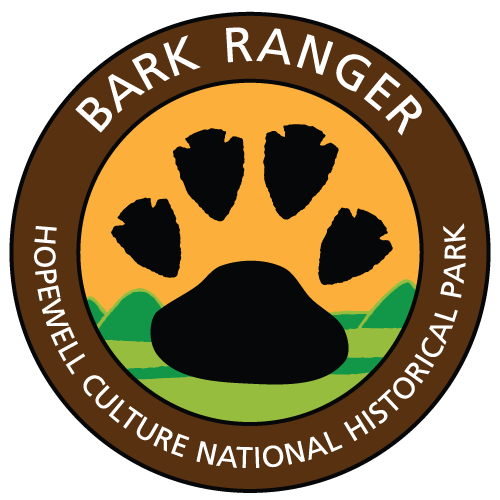 Circular logo with a large black paw print over green hills and an orange sky, labeled Bark Ranger.