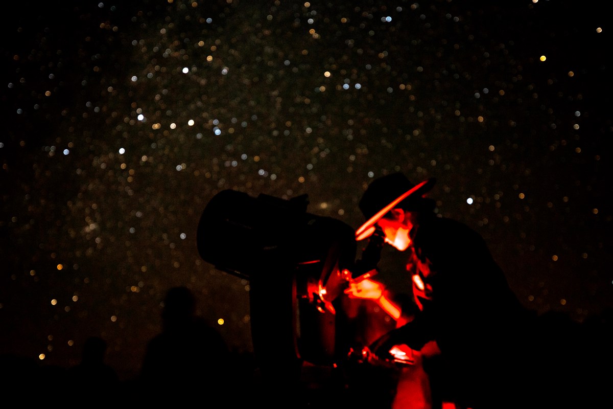 Ranger viewing the night sky through a telescope with numerous stars visible above her
