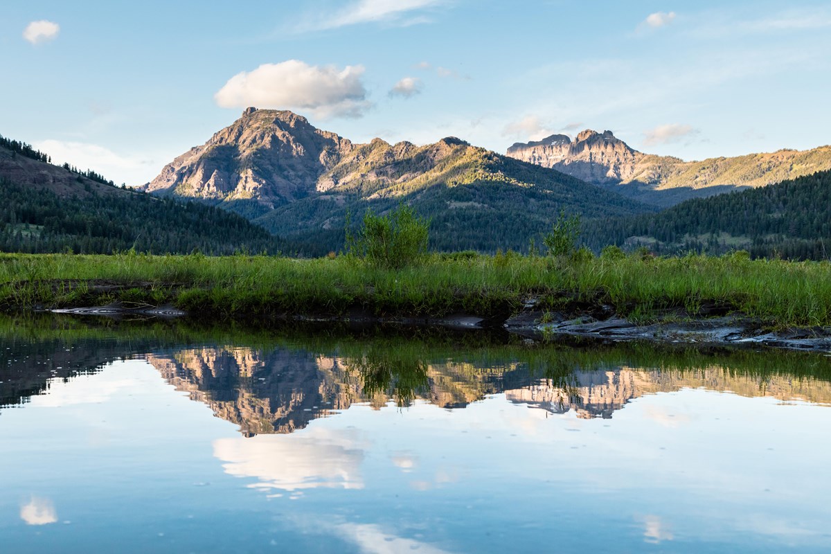 Dramatic mountains and blue sky are reflected in clear stream water