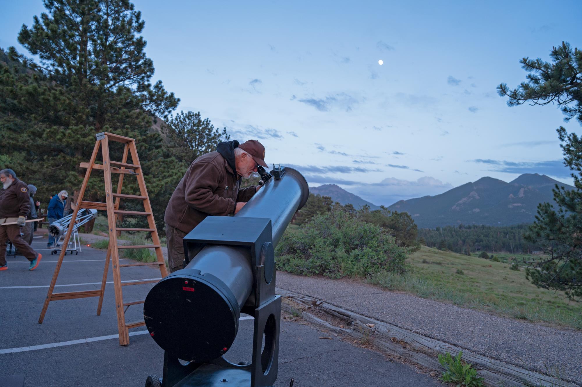 An NPS volunteer is looking up at the night sky with a telescope