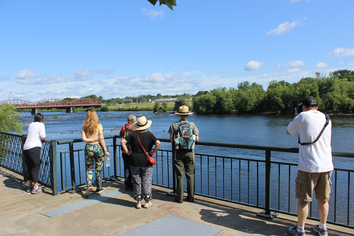 A small group of visitors and a uniformed park ranger looking out at the Merrimack River.