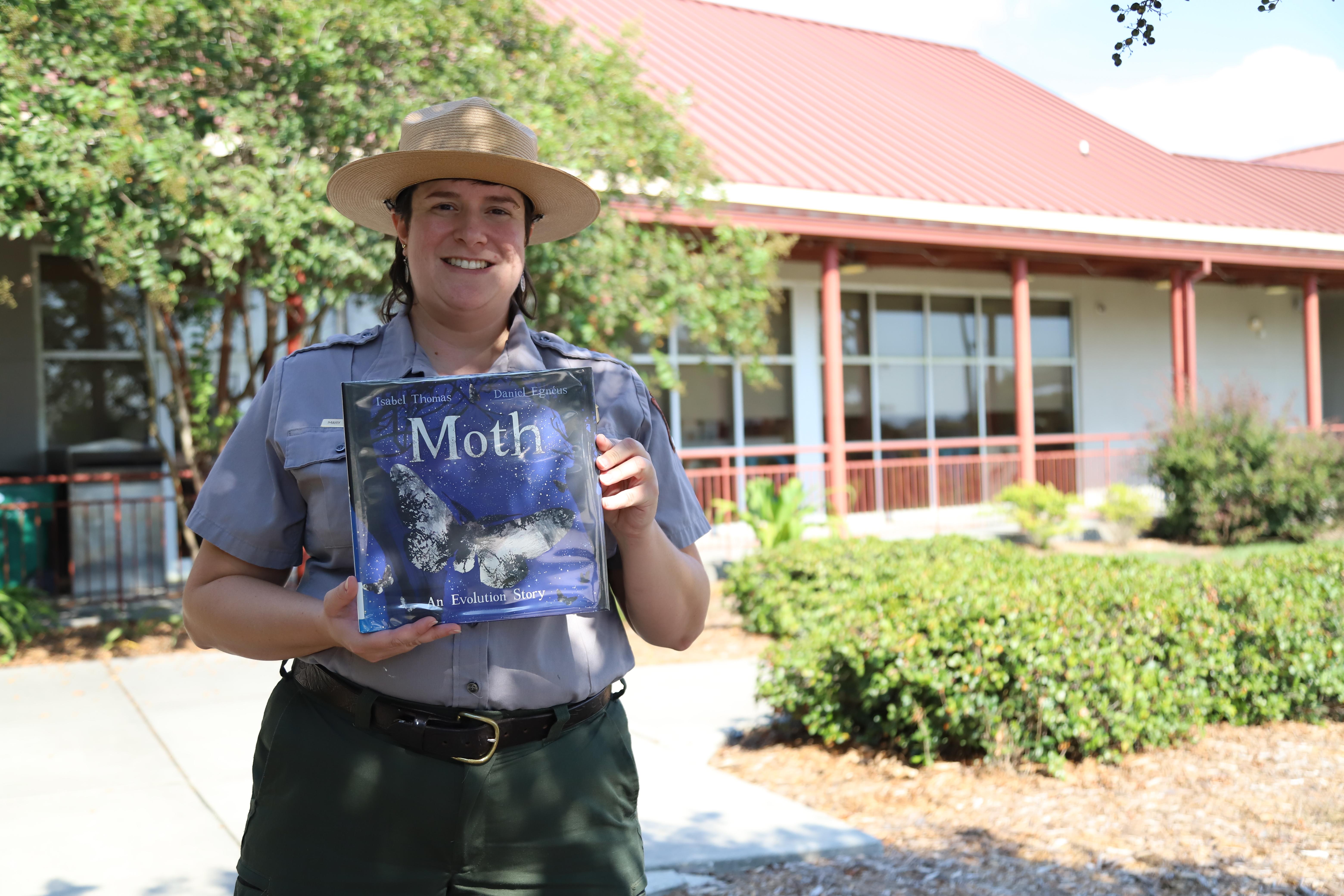 Park Ranger holding a children's book standing outside of Lafitte Library