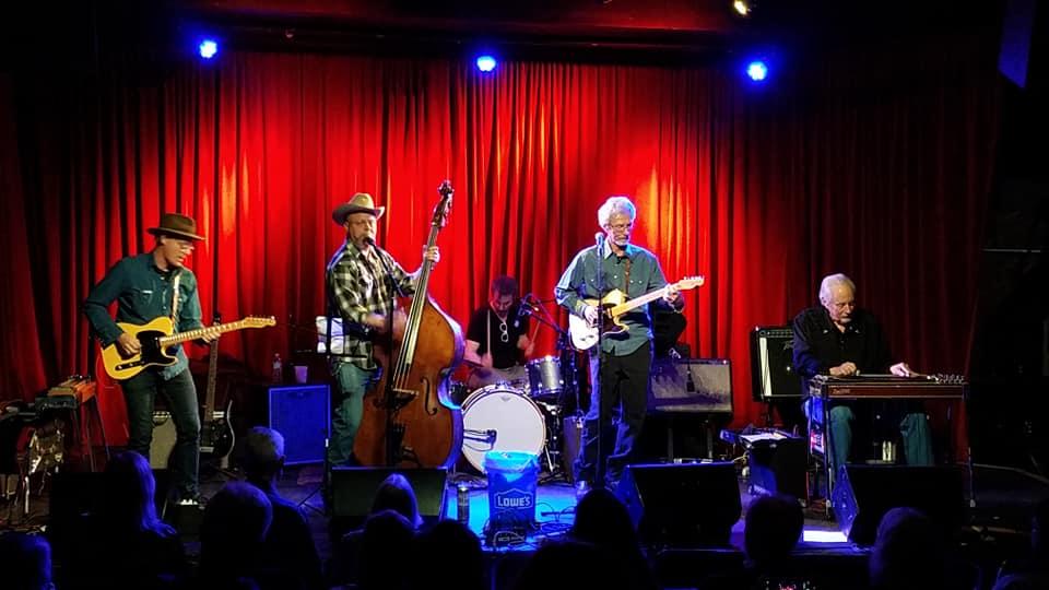 Five musicians on a stage against a red curtain