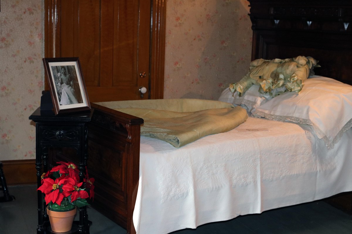 Gold colored gown laying across historic bed, black & white photo on table, poinsettia on floor