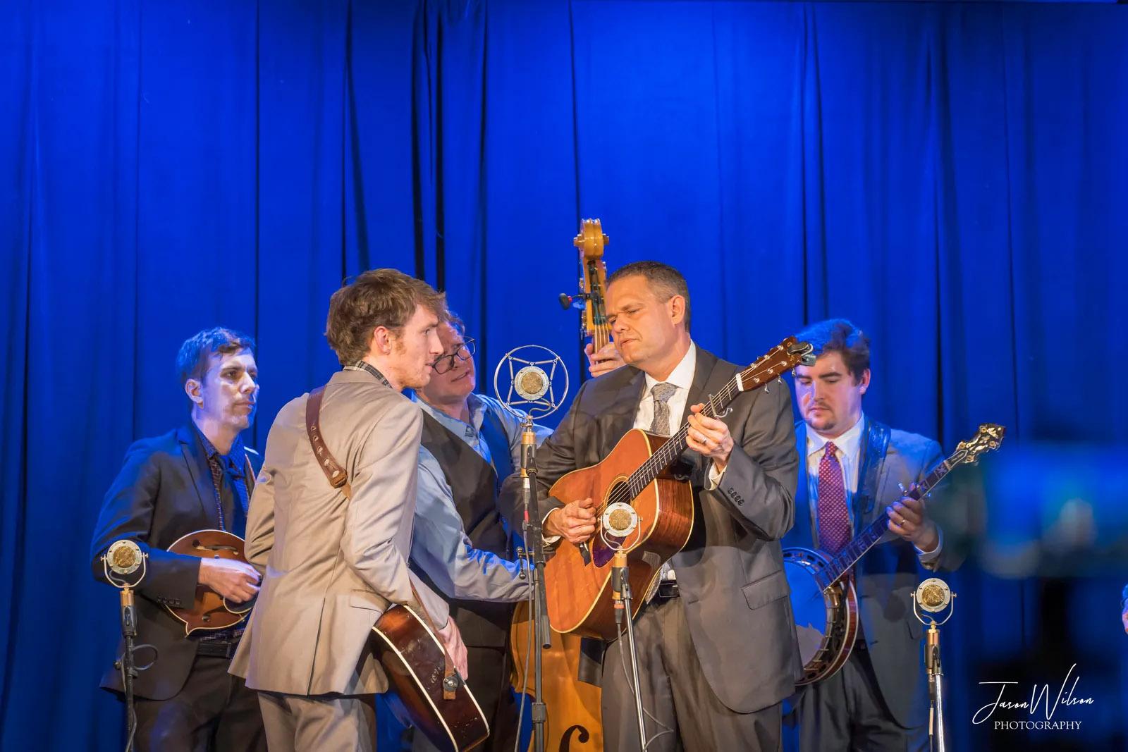 Five musicians performing in front of a blue curtain