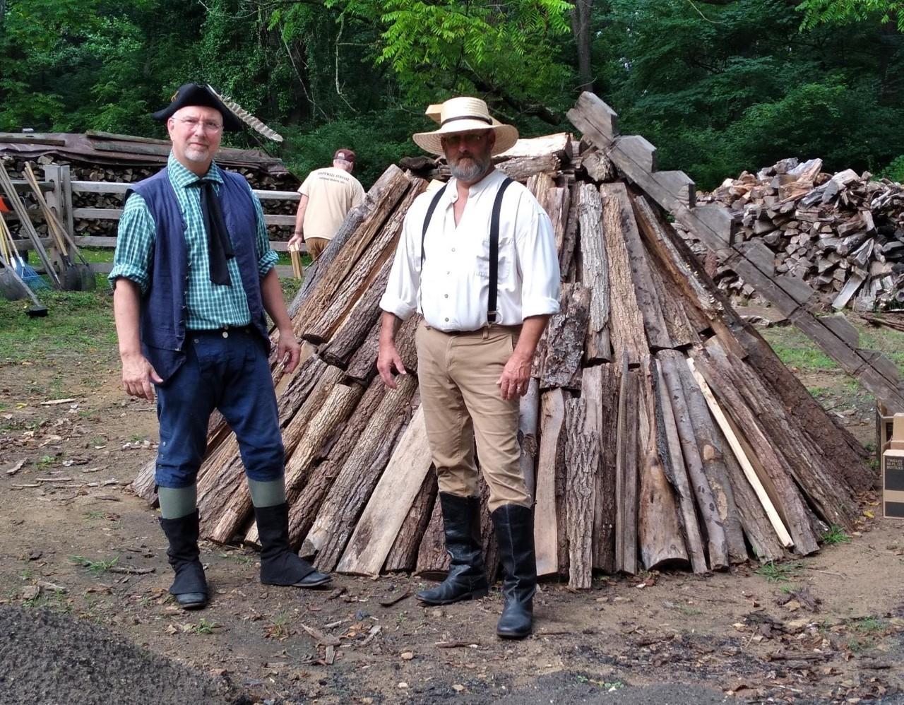 Volunteers in historic clothing stand next to charcoal pit