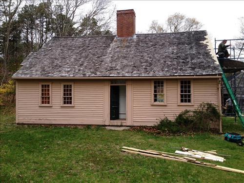 Brown Cape Cod style home with a brick chimney standing up in the middle of the roof.
