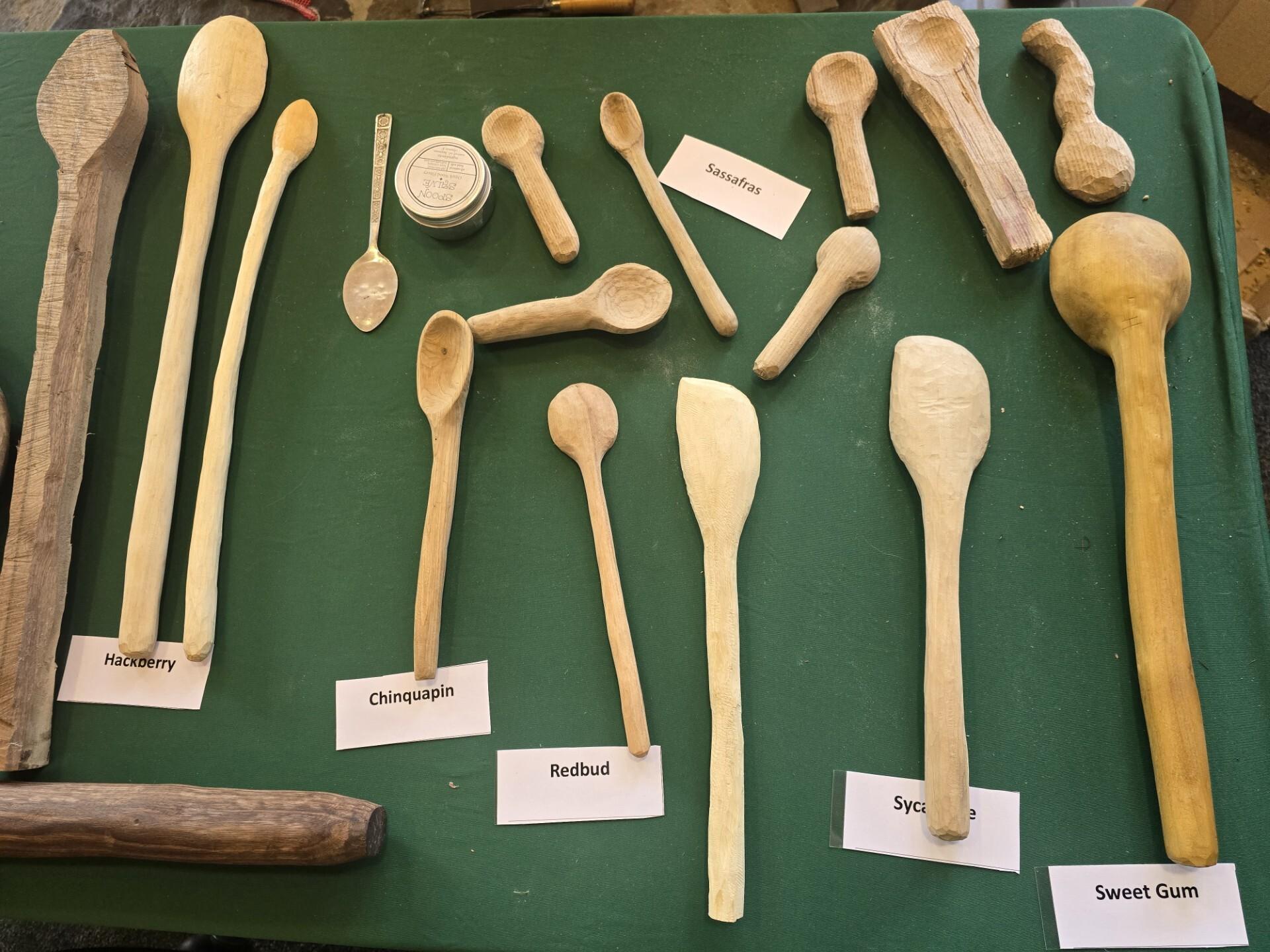Several whittled, wooden spoons are spread out on a green tablecloth.