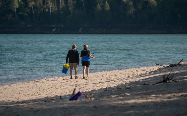 Two people collecting litter from a scenic beach.