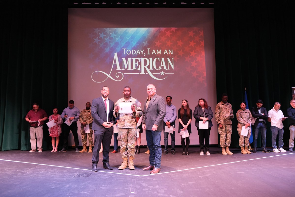 New United States citizens stand on stage after taking their oath of citizenship.