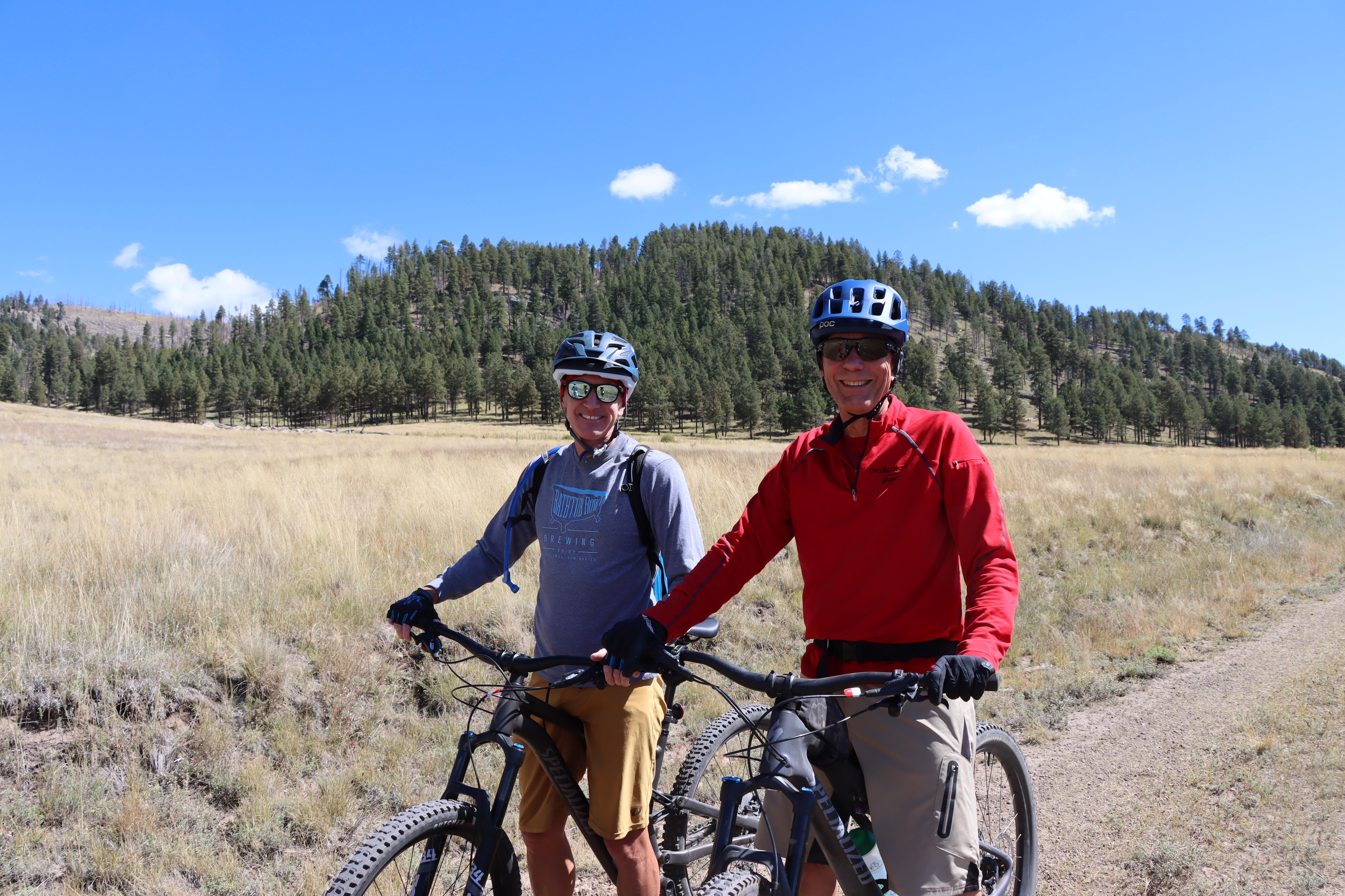 Two cyclists pause for a photo on a two-track road in a montane grassland.